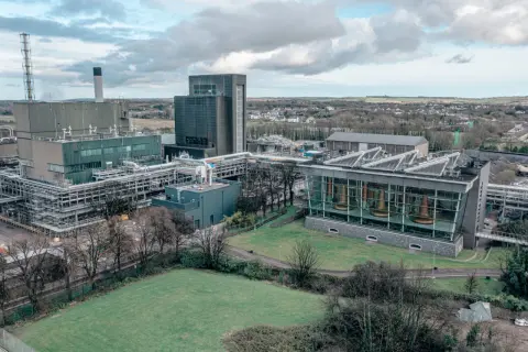 Vue aérienne de la distillerie Midleton, avec ses bâtiments industriels, ses cuves en cuivre visibles à travers une façade vitrée, et un paysage verdoyant en arrière-plan.