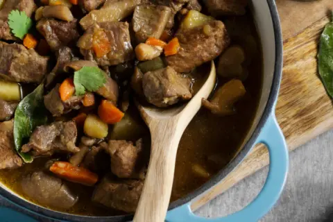 Un savoureux navarin d'agneau, aux carottes et pommes de terre, mijote dans une cocotte bleue. Son origine est un délice.
