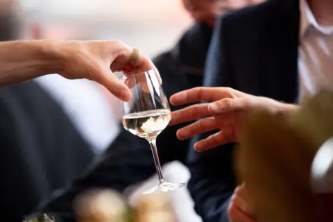 Des mains échangent un verre de vin blanc lors d'une dégustation à Angers.