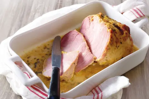 Palette à la diable, tranchée et servie dans un plat blanc avec une sauce dorée. Un couteau est posé sur la viande.