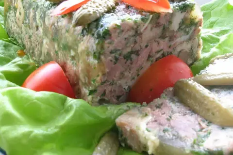 Tranche de pâté de tête maison, garnie de persil, servie sur des feuilles de laitue avec des tomates et des cornichons. Un délice pour une recette de pâté de tête.