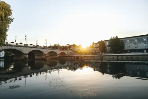 Un pont de pierre traverse une rivière calme, reflétant le soleil couchant sur les bâtiments historiques. Une belle vue pour savoir quoi faire à Cognac.