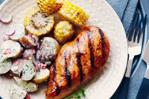 Un délicieux poulet grillé au sirop d'érable, servi avec une salade de pommes de terre crémeuse et des épis de maïs rôtis.