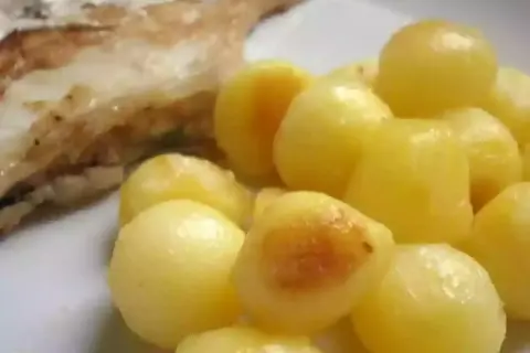 Une assiette de poisson grillé avec une généreuse portion de pomme de terre parisienne, dorée et appétissante.