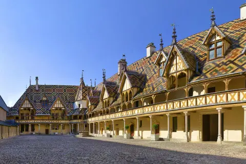 Cour intérieure des Hospices de Beaune, un joyau architectural à visiter. Toits colorés, arcades et pavés de pierre.