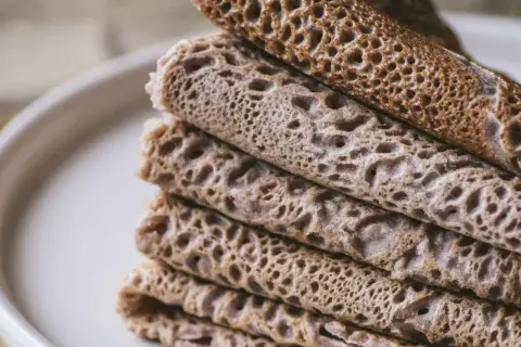 Pile de crêpes et de galettes, certaines roulées, d'autres pliées, avec une texture alvéolée. Un délice qui rappelle le goût de l'andouille.