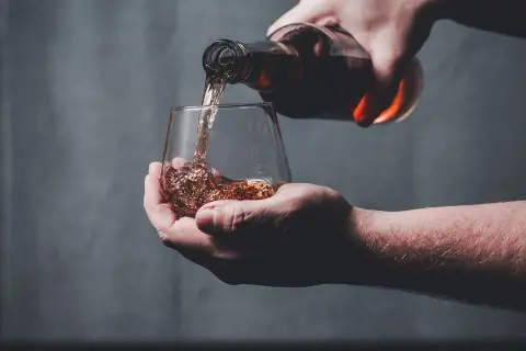 Une main verse un liquide ambré dans un verre, peut-être le pire whisky jamais goûté.