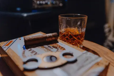 Un verre de whisky ambré et un cigare posés sur une boîte de cigares, prêts pour un moment de détente.