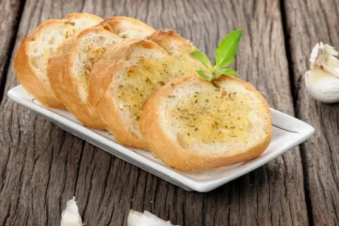 Tranches de pain grillé à l'ail, garnies d'herbes, rappelant la préfou recette traditionnelle. Une tête d'ail repose à côté.