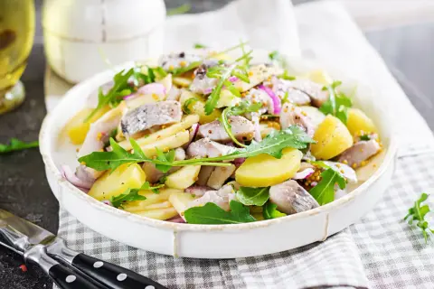 Salade de pommes de terre et hareng à l'huile, garnie de roquette et d'oignons rouges. Une recette simple et savoureuse.
