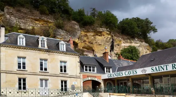 La maison Lacheteau, avec ses façades en pierre et ses toits d'ardoise, se dresse au pied d'une falaise rocheuse.