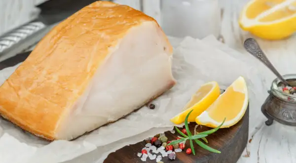 Un beau morceau de haddock fumé, prêt pour la cuisson, accompagné de quartiers de citron, de romarin et d'un mélange de poivre et de sel.