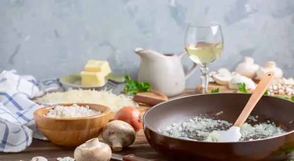 Préparation d'une sauce au vin blanc pour viande : oignons dans une poêle, riz, champignons, beurre, parmesan et vin blanc.