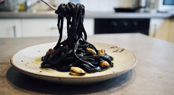 Pâtes noires, colorées avec de l'encre de seiche, c'est quoi ce plat savoureux ? Elles sont servies avec des moules sur une assiette.