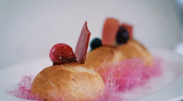 Un ou une profiterole décoré d'une framboise, d'une tuile de chocolat et de barbe à papa rose.