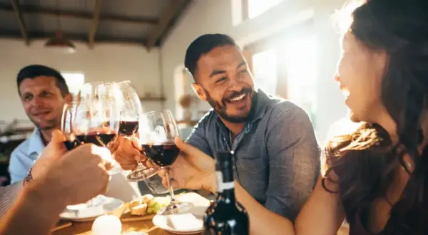 Des amis trinquent avec des verres de vin rouge lors d'une soirée dégustation vin conviviale, riant sous le soleil.