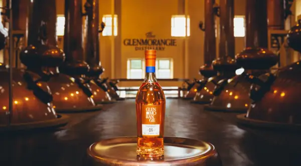 Bouteille de whisky Glenmorangie 18 ans posée sur un plateau en cuivre, au cœur de la distillerie Glenmorangie, entourée d'alambics en cuivre.