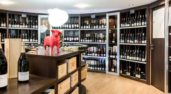 Une cave à vin bien garnie, avec une statue de taureau rouge au centre. Des bouteilles de champagne et de vin sont exposées sur des étagères.