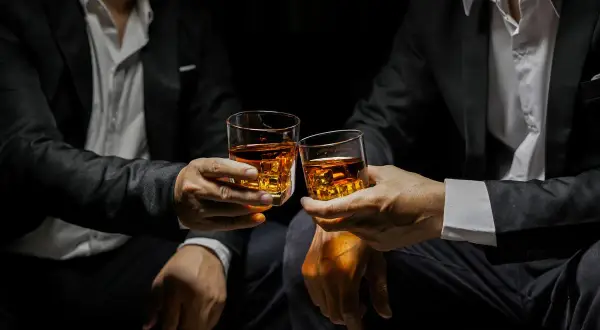 Deux hommes en costume portent des verres de whisky ambré, évoquant la définition d'un single malt : pur, authentique, une expérience unique.