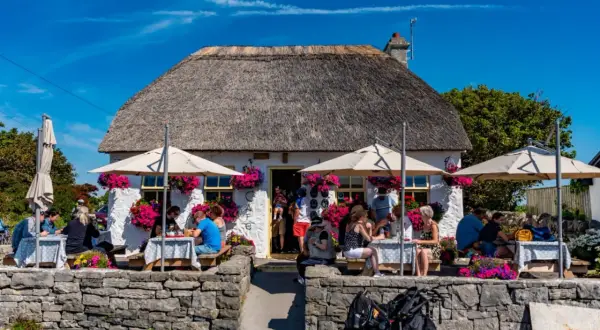 Café pittoresque avec toit de chaume, parasols et fleurs. Des gens dégustent un repas en plein air, peut-être un délicieux aran poisson.