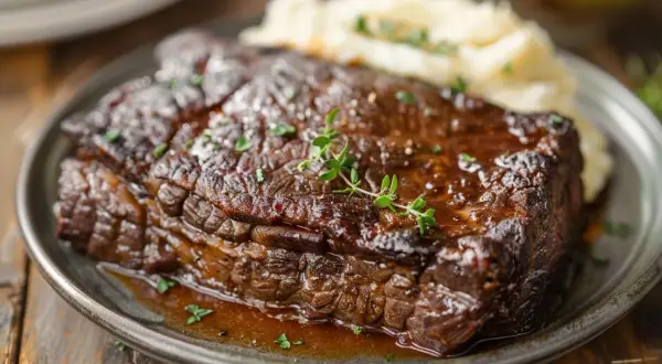 Un plat de boeuf braisé, tendre et juteux, servi avec une purée de pommes de terre crémeuse et garni de thym frais.