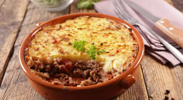 Un plat de hachis parmentier, un classique du repas français, servi dans un plat en terre cuite sur une table en bois.