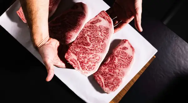 Des mains présentent des steaks de bœuf persillés, marbrés de gras, promettant le meilleur bœuf du monde.