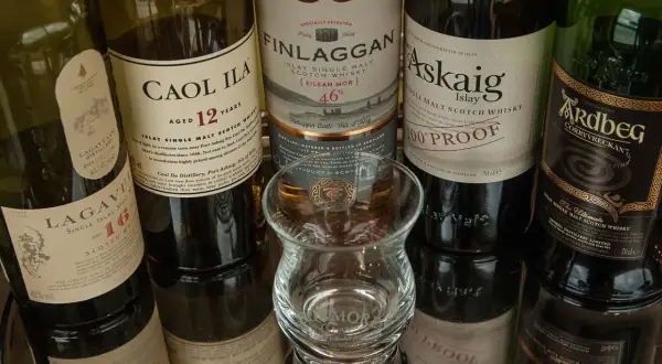 Bouteilles de whisky Islay tourbé : Caol Ila, Lagavulin, Finlaggan, Port Askaig, Ardbeg. Un verre à dégustation vide est au centre.