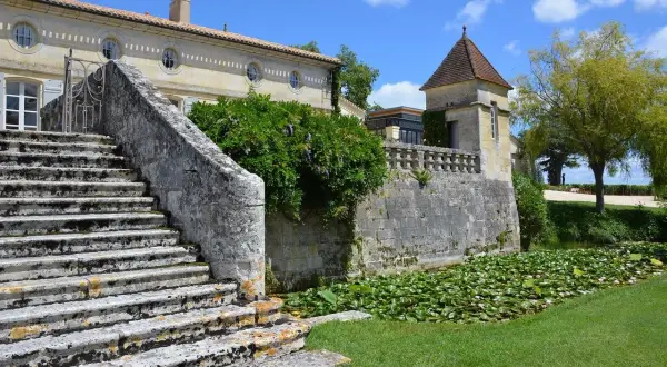 Escalier de pierre menant à un château, avec un étang de nénuphars. Une belle journée pour une visite château Pomerol.