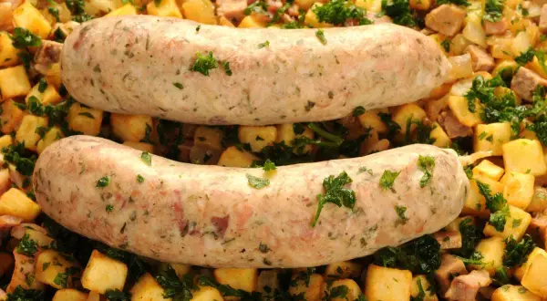 Deux andouillettes au four, dorées et savoureuses, reposent sur un lit de pommes de terre sautées et de persil frais. Un plat réconfortant prêt à être dégusté.