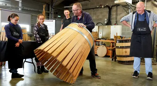 Visite tonnellerie Bourgogne : un maître tonnelier montre un fût en cours de fabrication à des apprentis.