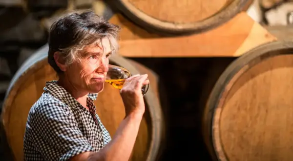 Une femme déguste un verre de vin de Pau, entourée de fûts de chêne dans une cave.