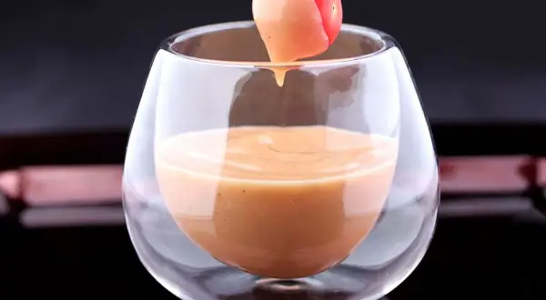 Une tomate cerise trempée dans une sauce cocktail onctueuse, servie dans un verre élégant.