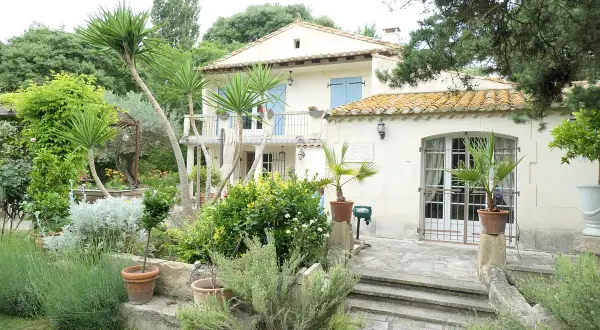 Maison en pierre avec jardin luxuriant, palmiers et lavande. Le panneau "Domaine des chênes truffiers" est visible.