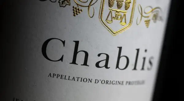Gros plan sur une étiquette de vin Chablis, avec un blason doré orné de grappes de raisin et d'une balance. L'appellation d'origine protégée est clairement visible.