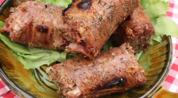 Trois andouillettes grillées au barbecue, servies sur un lit de laitue dans une assiette décorative.