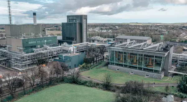 Vue aérienne de la distillerie Midleton, avec ses bâtiments industriels, ses cuves en cuivre visibles à travers une façade vitrée, et un paysage verdoyant en arrière-plan.