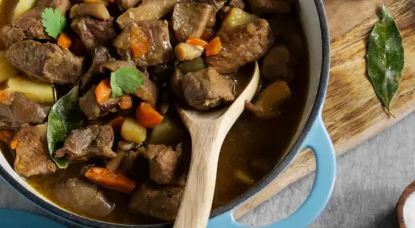 Un savoureux navarin d'agneau, aux carottes et pommes de terre, mijote dans une cocotte bleue. Son origine est un délice.