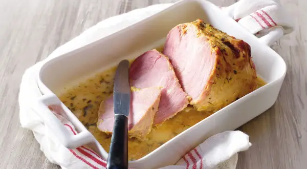 Palette à la diable, tranchée et servie dans un plat blanc avec une sauce dorée. Un couteau est posé sur la viande.