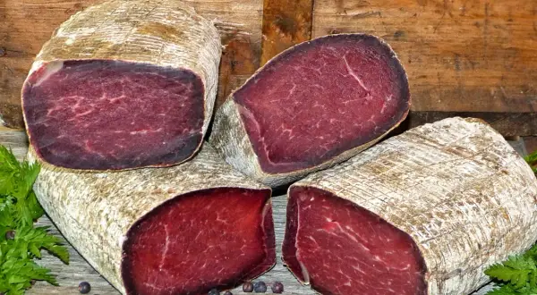 Quatre morceaux de viande des Grisons, d'origine suisse, sont présentés sur un fond de bois. La viande est rouge foncé, avec une texture fibreuse.