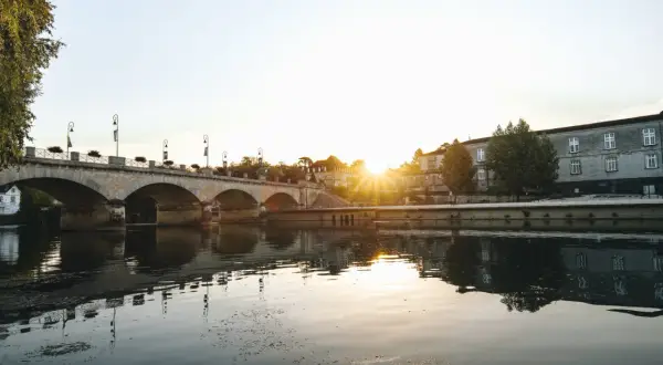 Un pont de pierre traverse une rivière calme, reflétant le soleil couchant sur les bâtiments historiques. Une belle vue pour savoir quoi faire à Cognac.