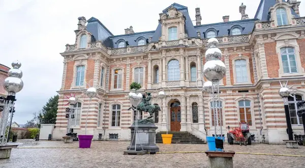 Devant un château, des sphères argentées, comme des habits de lumière, scintillent sur des structures métalliques, entourant une statue équestre.
