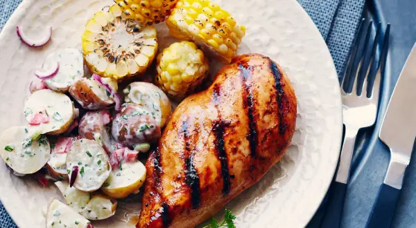 Un délicieux poulet grillé au sirop d'érable, servi avec une salade de pommes de terre crémeuse et des épis de maïs rôtis.