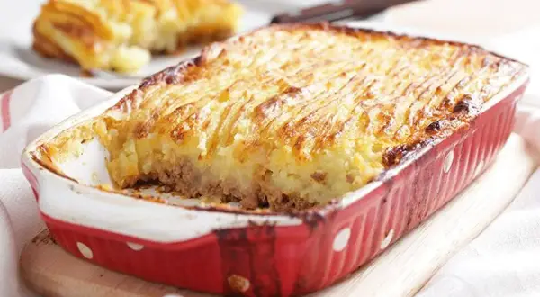 Un plat de hachis parmentier, dont l'origine remonte à Antoine-Augustin Parmentier, est servi dans un plat rouge à pois blancs.