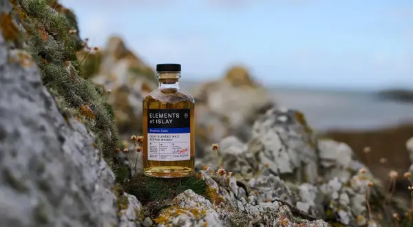 Bouteille de whisky "Elements of Islay" posée sur des rochers moussus, évoquant l'atmosphère sauvage de la distillerie Islay.