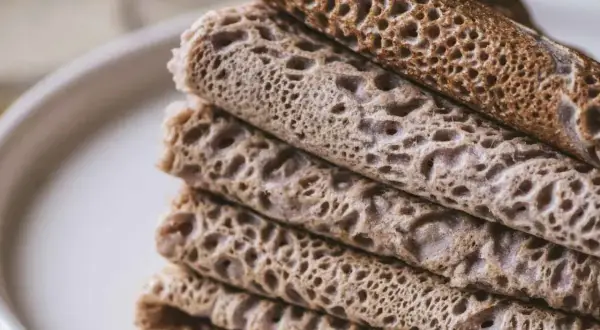 Pile de crêpes et de galettes, certaines roulées, d'autres pliées, avec une texture alvéolée. Un délice qui rappelle le goût de l'andouille.