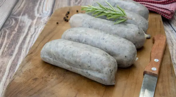 Saucisses grises sur planche en bois, avec romarin et poivre. La différence entre andouille et andouillette est subtile, mais la texture ici suggère une andouillette.