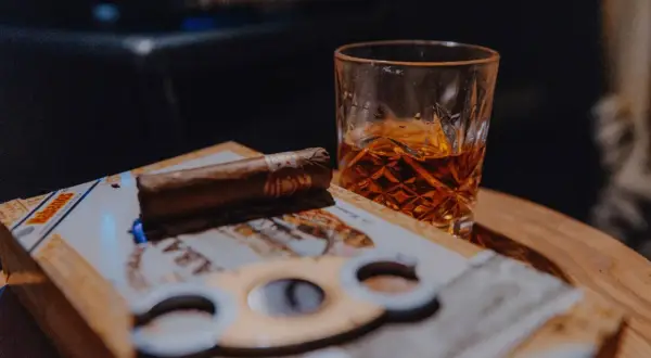 Un verre de whisky ambré et un cigare posés sur une boîte de cigares, prêts pour un moment de détente.