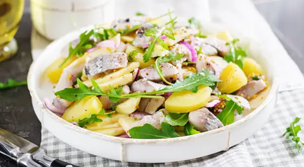 Salade de pommes de terre et hareng à l'huile, garnie de roquette et d'oignons rouges. Une recette simple et savoureuse.