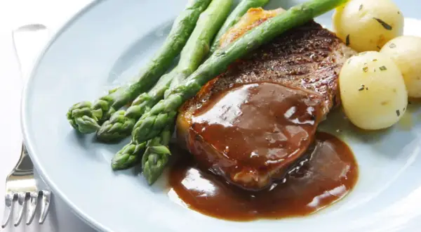 Un délicieux steak servi avec une sauce onctueuse, des asperges croquantes et des pommes de terre nouvelles. Un plat parfait pour un dîner savoureux.